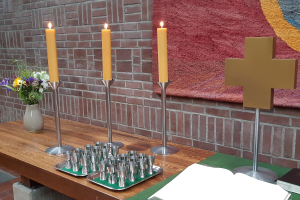 Altar der Johannesgemeinde, bunter Blumenstrauß, 3 brennende Kerzen, davor 2 Tablets mit Einzelkelchen für das Abendmahl, daneben das Kreuz und davor die aufgeschlagene Bibel