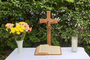 Altar im Garten der Johanneskirche. Weiße Tischdecke, links Blumenstrauß, mitte Kreuz und Bibel, rechts Kerze, im Hintergrund grüne Hecke.