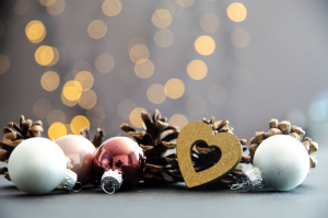 Vier Weihnachtskugeln, Tannenzapfen und ein goldenes Herz, im Hintergrund Lichtreflexe.