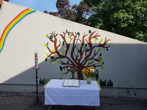 Altar mit Tischdecke und Kreuz im Atrium des Gemeindezentrums vor einer bemalten Wand