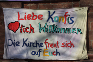 Willkommensgruß für die neuen Konfis in bunten Buchstaben auf einem großen Tuch an der Kirchenwand