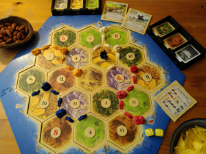 Spielbrett des Gesellschaftsspiels "Die Siedler" mit Spielkarten und Snacks am Rand.