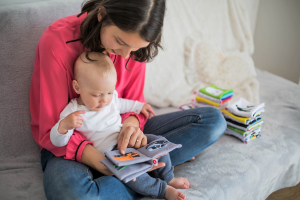 Mutter mit Baby auf dem Schoß. Mutter schaut gemeinsam mit Kind in ein Buch.
