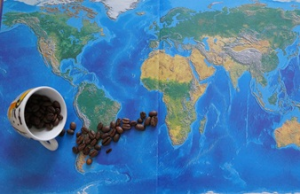 Umgekippte Kaffeetasse, aus der sich Kaffeebohnen über eine Weltkarte verteilen