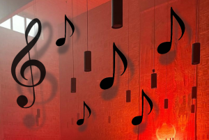 Collage mit Notenschlüssel und Noten, die zwischen den schwarzen Lampen der Johanneskirche vor den in rotes Licht getauchten Wänden schweben