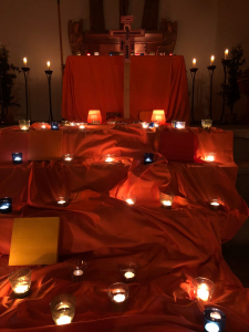 Kerzen vor Altar, orangene Tücher als Deko