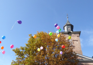 Aufsteigende, bunte Luftballons vor der Ev. Kirche