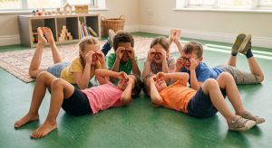 Kinder liegen im Kreis auf dem Boden und formen mit den Händen "Ferngläser" vor den Augen