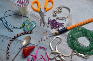 Bastelmaterial: Schere, Perlen, Schnur, Lineal verstreut auf einem Tisch