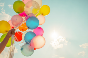 Viele farbige Ballons, die von einer Hand an Schnüren gehalten werden